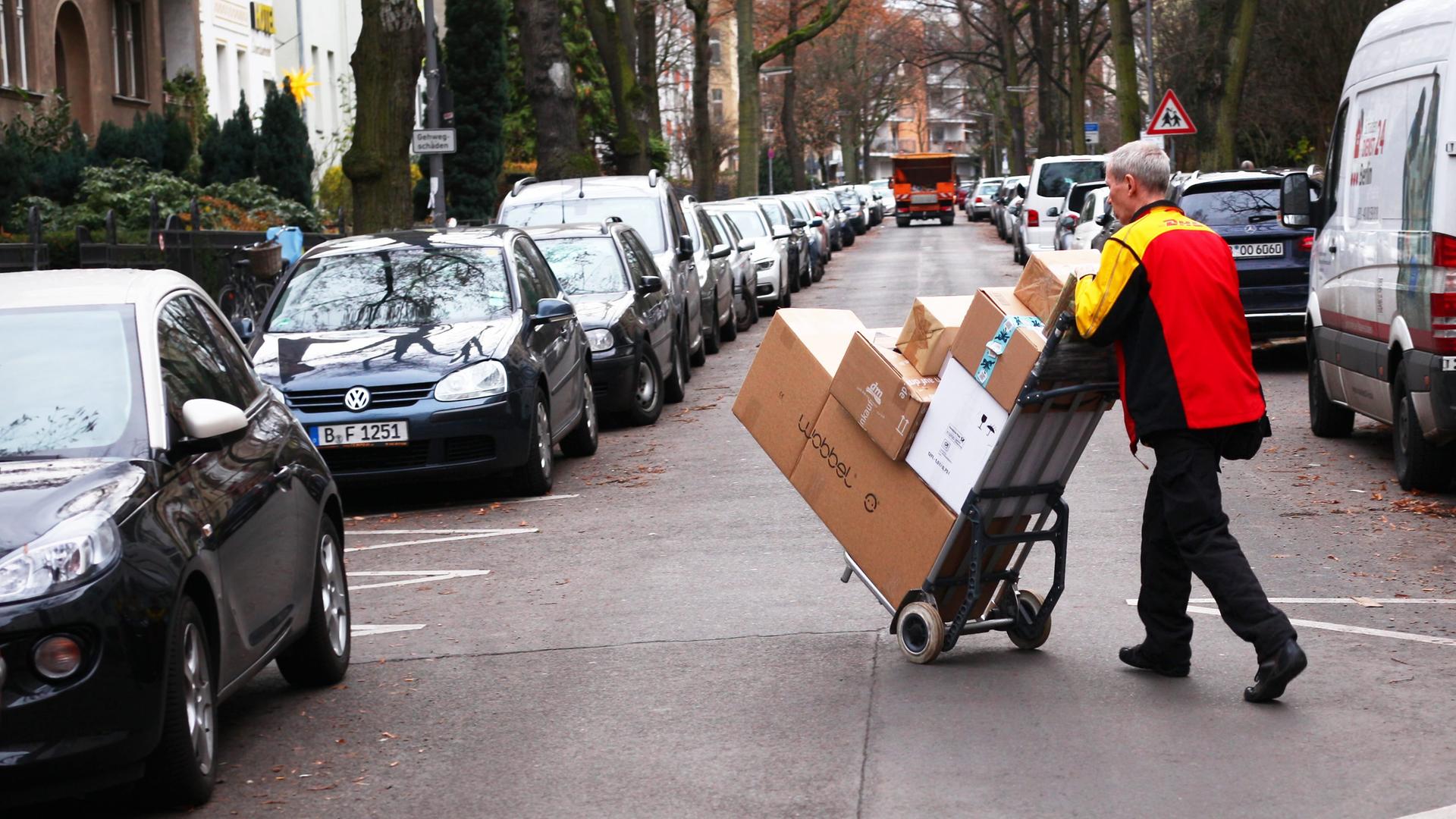 Ein Paketbote von Deutsche Post DHL bringt Päckchen und Pakete mit Hilfe einer Sackkarre über eine Straße. Ein Paketbote von Deutsche Post DHL bringt Päckchen und Pakete mit Hilfe einer Sackkarre über eine Straße.