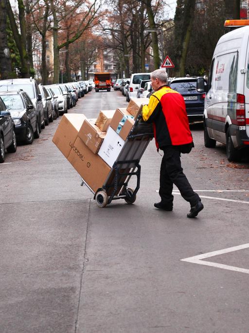 Ein Paketbote von Deutsche Post DHL bringt Päckchen und Pakete mit Hilfe einer Sackkarre über eine Straße.