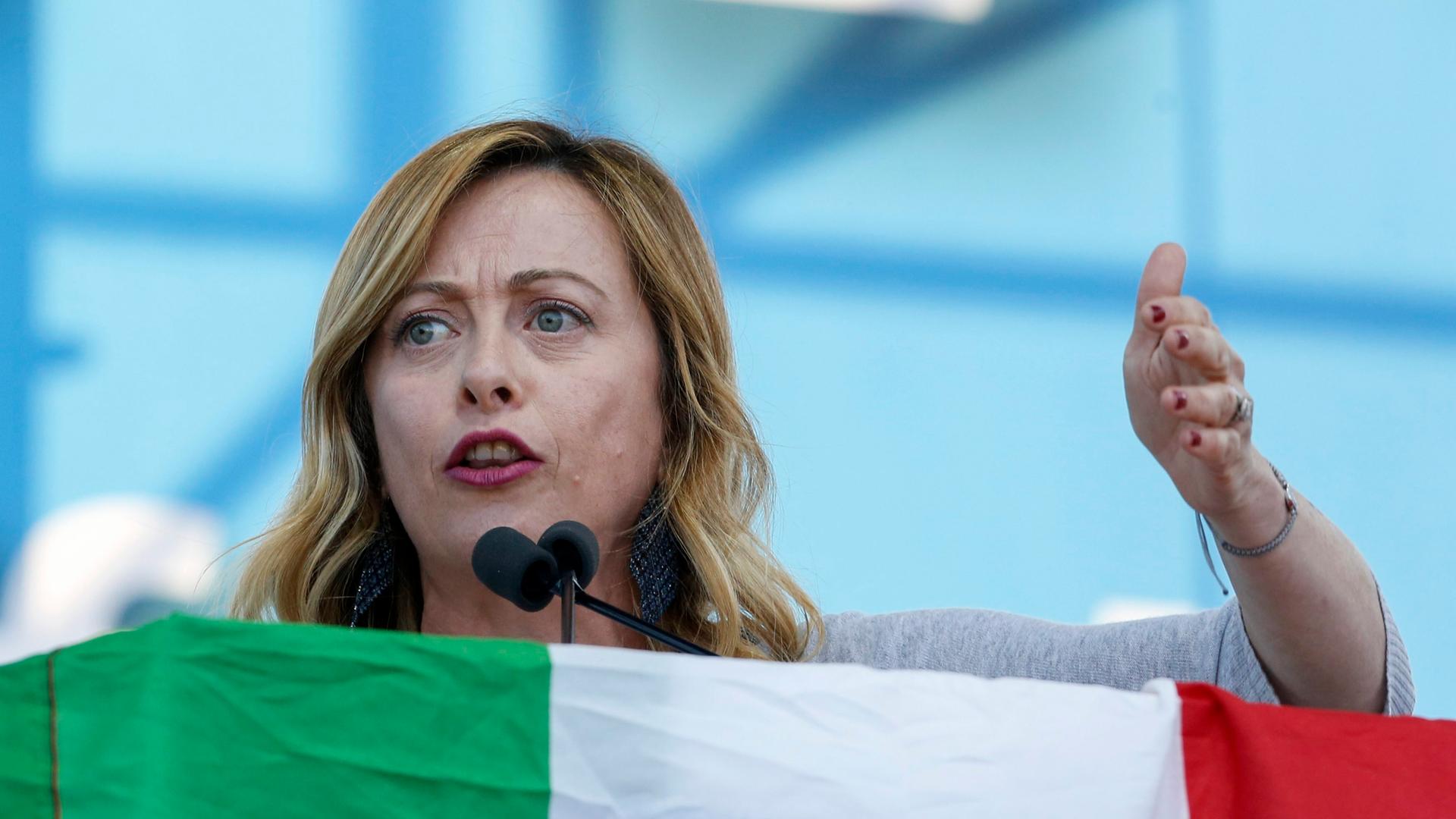 Giorgia Meloni spricht an einem Pult, welches mit der italienischen Fahne verhangen ist.
