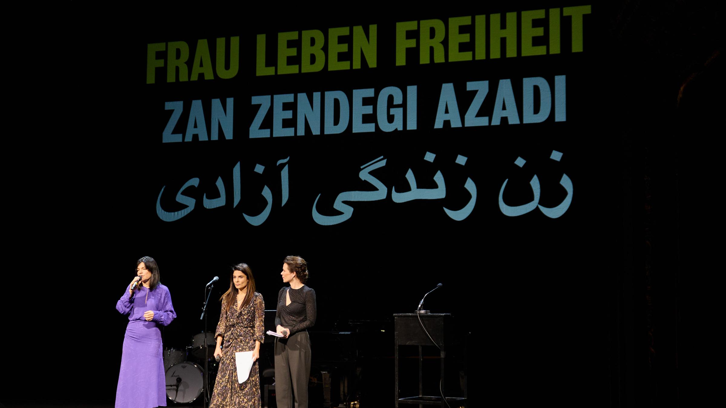 Die Schauspielerinnen Jasmin Tabatabai (l-r), Sarah Sandeh und Melika Foroutan stehen auf einer Bühne, hinter ihnen ein Banner mit der Aufschrift "Frau Leben Freiheit"
