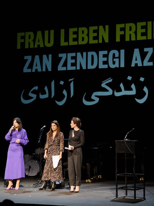 Die Schauspielerinnen Jasmin Tabatabai (l-r), Sarah Sandeh und Melika Foroutan stehen auf einer Bühne, hinter ihnen ein Banner mit der Aufschrift "Frau Leben Freiheit"
