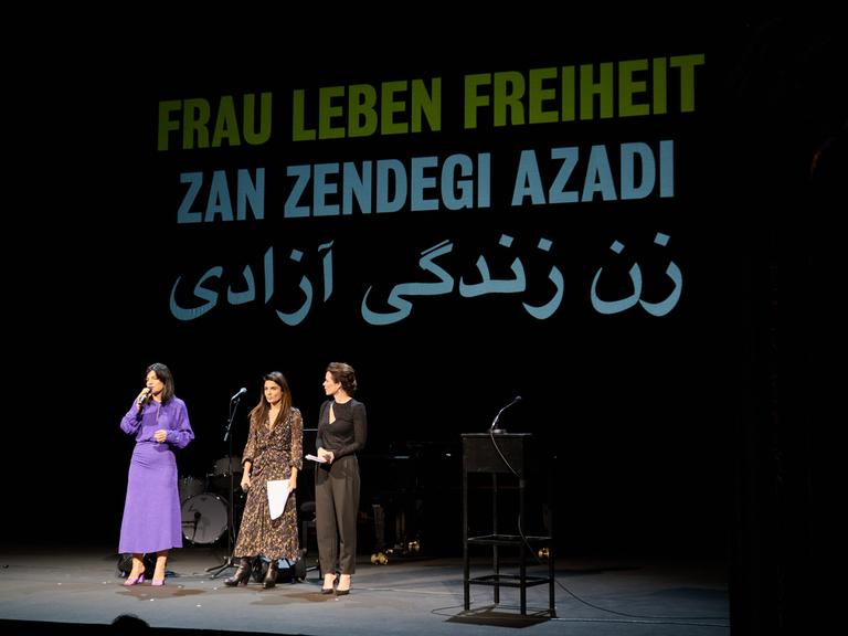 Die Schauspielerinnen Jasmin Tabatabai (l-r), Sarah Sandeh und Melika Foroutan stehen auf einer Bühne, hinter ihnen ein Banner mit der Aufschrift "Frau Leben Freiheit"
