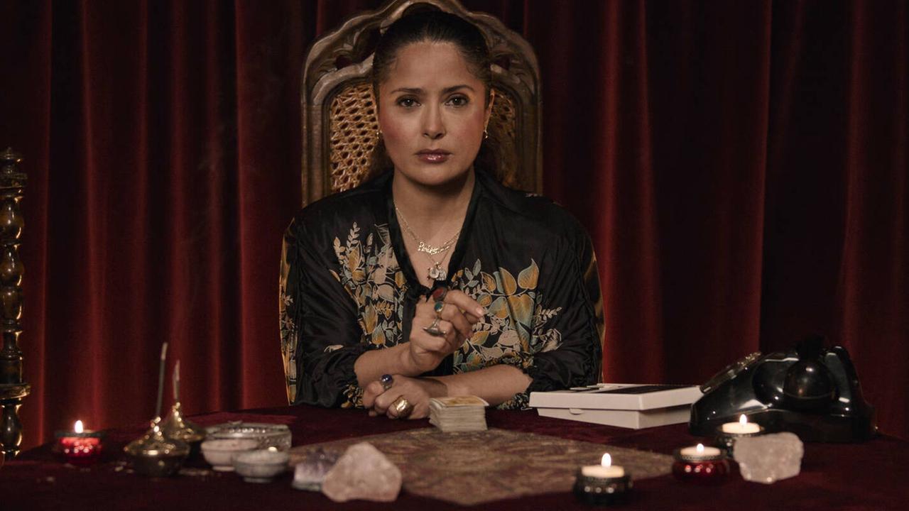 Die Schauspielerin Salma Hayek als Pina Auriemma in dem Film "House of Gucci" von Regisseur Ridley Scott. Sie sitzt an einem Tisch und schaut in die Kamera. Die Schauspielerin Salma Hayek als Pina Auriemma in dem Film "House of Gucci" von Regisseur Ridley Scott. Sie sitzt an einem Tisch und schaut in die Kamera.