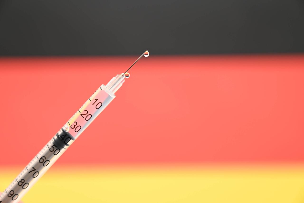 Eine Impfspritze vor einer nur unscharf zu sehenden Deutschland-Fahne Eine Impfspritze vor einer nur unscharf zu sehenden Deutschland-Fahne