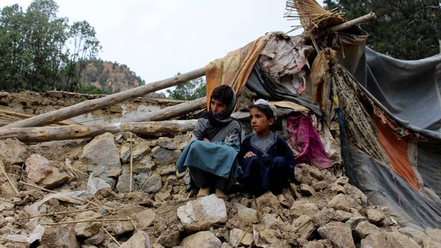 Zwei Jungen sitzen vor einem kaputten Haus in dem Land Afghanistan. Dort gab es ein schweres Erd-Beben. 
