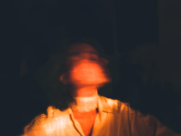 Verschwommene Darstellung einer Frau vor dunklem Hintergrund