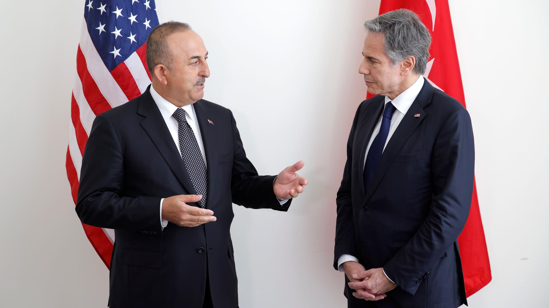 Zwei Männer stehen nebeneinander und unterhalten sich, hinter ihnen hängen die Fahnen der USA und der Türkei.