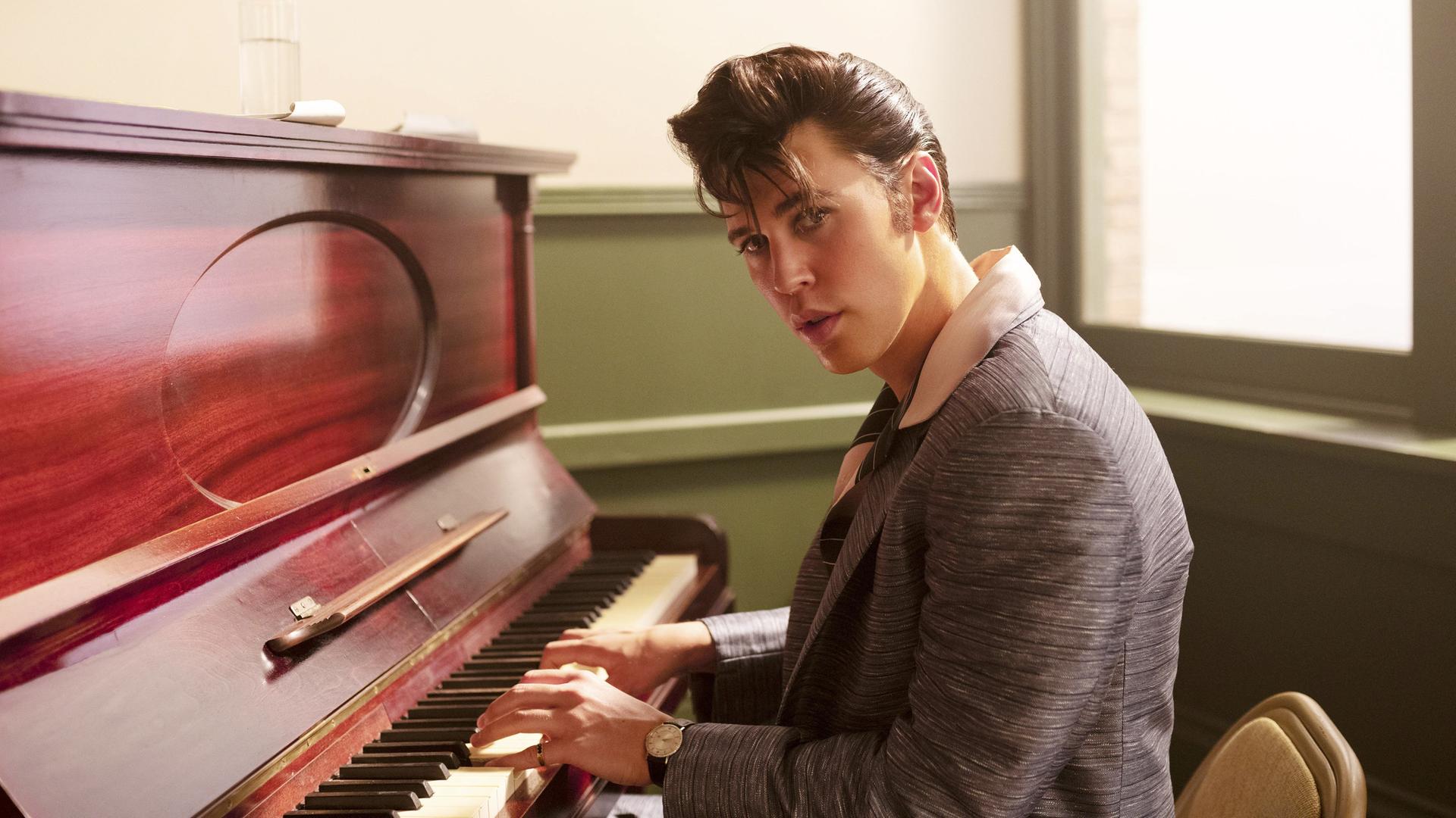 Filmstill aus "Elvis" von Baz Luhrmann. Der Schauspieler Austin Butler sitzt als Elvis am Klavier, 2022. Filmstill aus "Elvis" von Baz Luhrmann. Der Schauspieler Austin Butler sitzt als Elvis am Klavier, 2022.