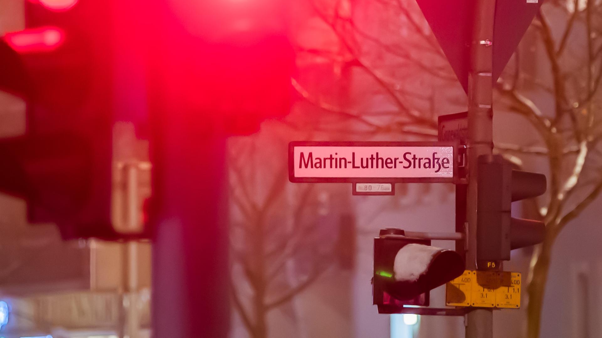 Das Straßenschild der Martin-Luther-Straße in Berlin-Schöneberg im Dunklen im Winter. Schnee liegt auf einer Ampel, eine andere zeigt rot.
