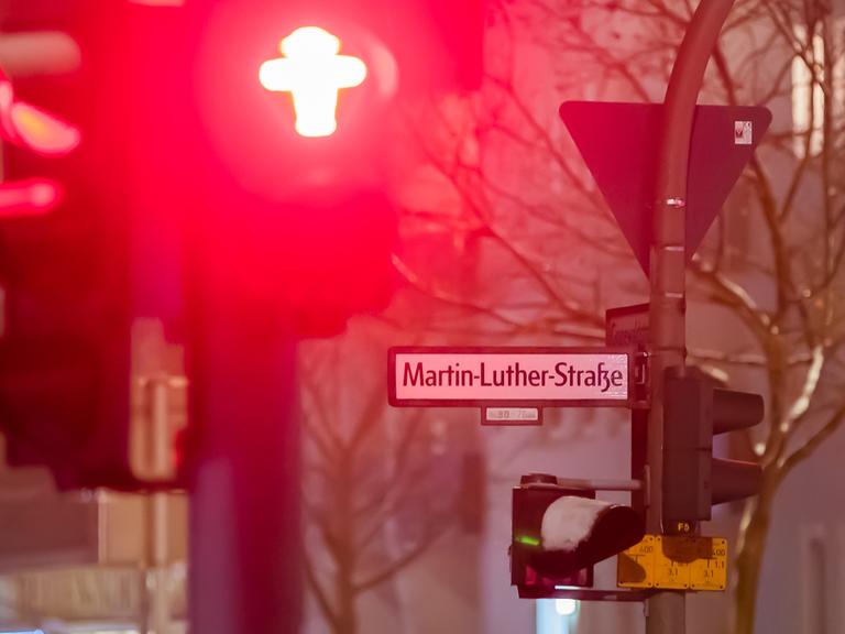 Das Straßenschild der Martin-Luther-Straße in Berlin-Schöneberg im Dunklen im Winter. Schnee liegt auf einer Ampel, eine andere zeigt rot.