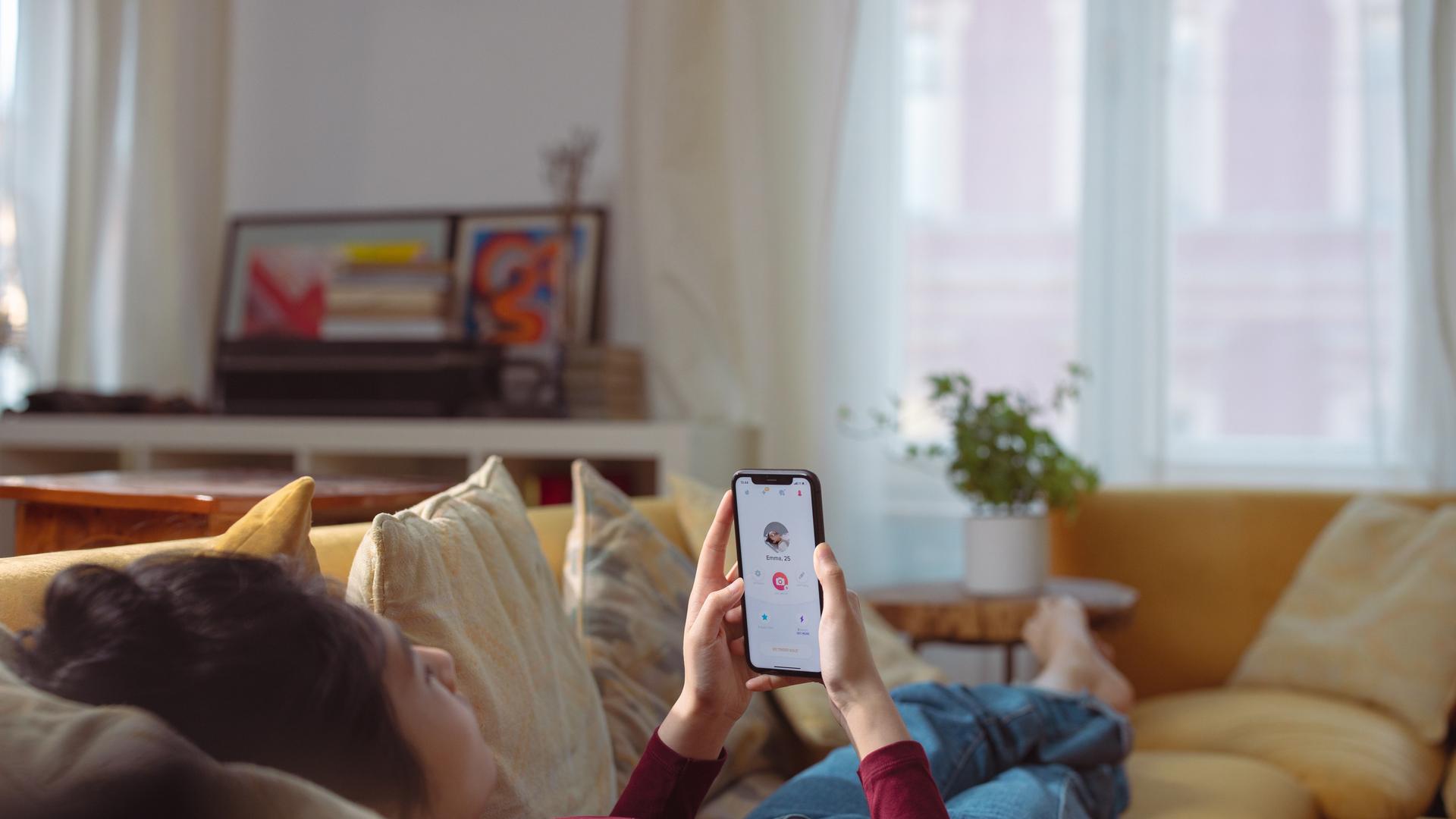 Eine Frau liegt auf dem Sofa und schaut in eine App auf ihrem Smartphone Eine Frau liegt auf dem Sofa und schaut in eine App auf ihrem Smartphone