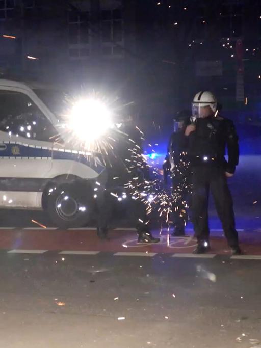 Polizeibeamte stehen in der Silvesternacht in Berlin hinter explodierendem Feuerwerk. 