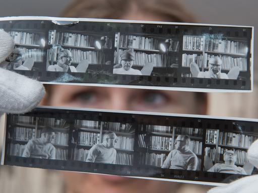 Andrea Werner, Mitarbeiterin im Wolfgang-Koeppen-Archiv (WKA) des Instituts für Deutsche Philologie an der Ernst-Moritz-Arndt Universität Greifswald, hält Kontaktabzüge von Wolfgang Koeppen in die Kamera. Sie trägt weiße Handschuhe, ihre Augen sind zwischen den Fotos zu sehen.