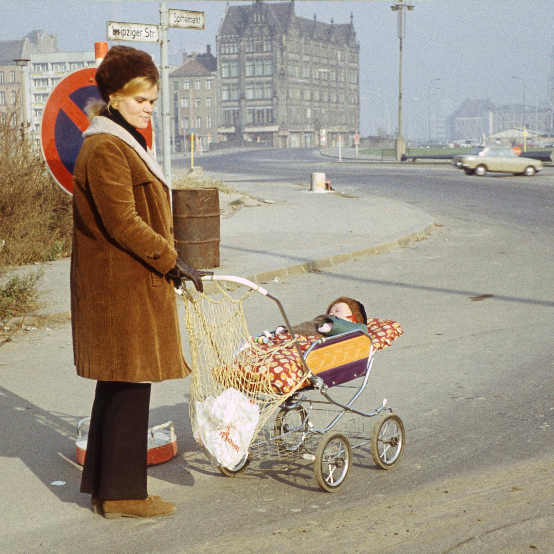 Eine Frau mit Kinderwagen, in dem ein Baby schläft, steht mit nachdenklichem Blick an der Ecke Leipziger Strasse / Am Spittelmarkt in Berlin 1973. Die Spuren des Kriegs sind noch im Stadtbild zu erkennen.