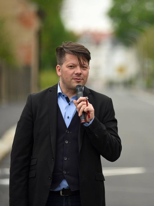Der Zittauer Oberbürgermeister Thomas Zenker steht mit Mikrofon in der Hand auf einer Straße.