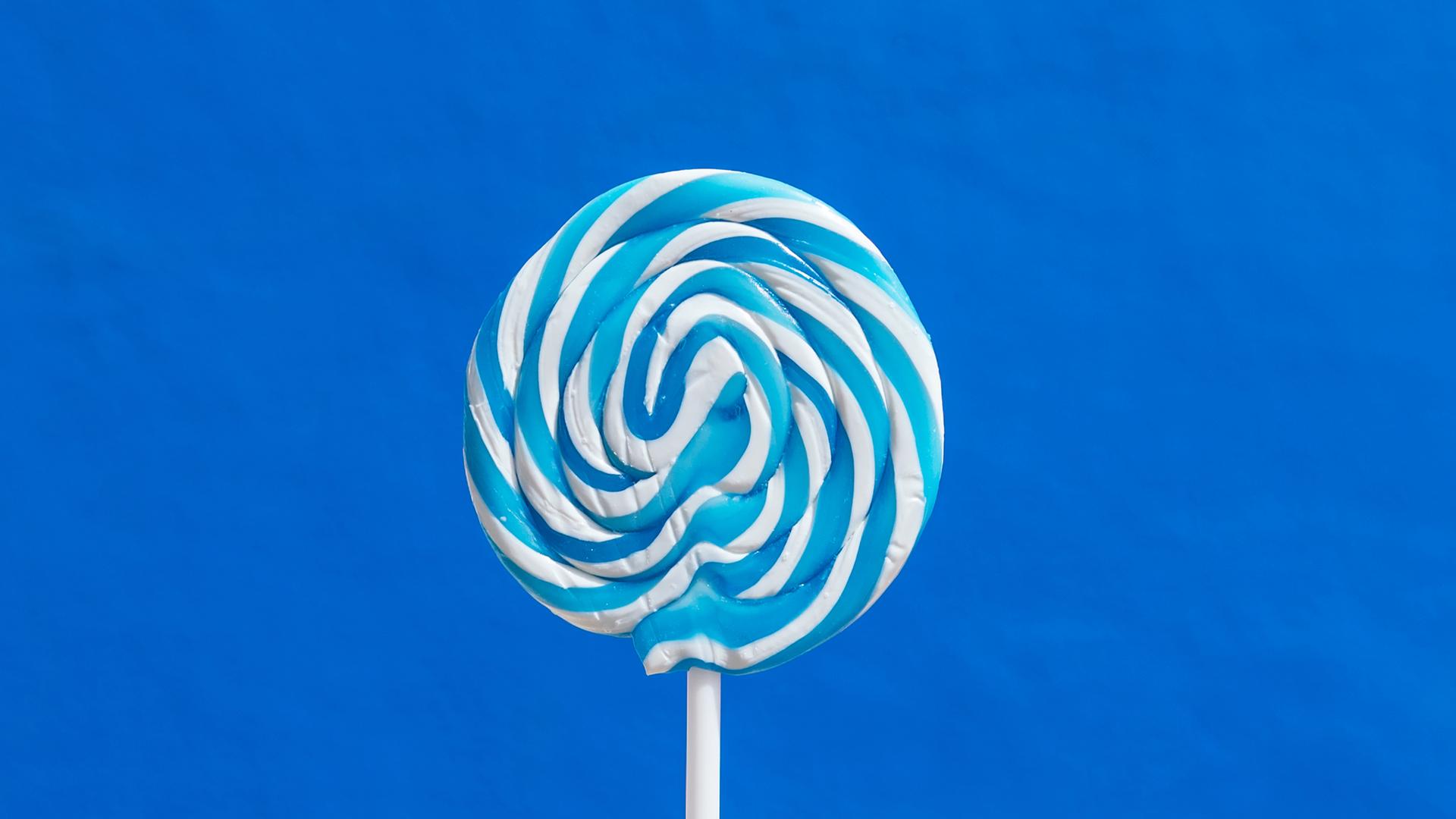 Ein blau-weißer Lutscher am Stil vor blauem Hintergrund. Ein blau-weißer Lutscher am Stil vor blauem Hintergrund.