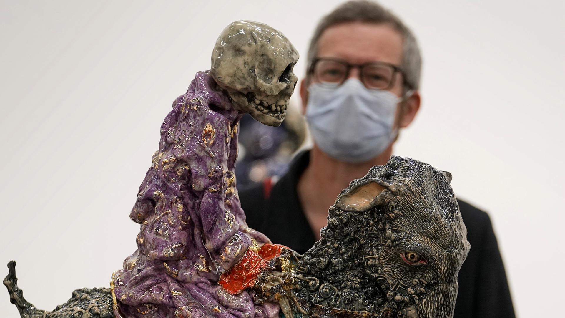 Ein Besucher mit Maske betrachtet auf der Art Cologne eine Arbeit von Carolein Smit aus den Niederlanden. Es ist ein auf einer Ziege reitendes Skelett. Ein Besucher mit Maske betrachtet auf der Art Cologne eine Arbeit von Carolein Smit aus den Niederlanden. Es ist ein auf einer Ziege reitendes Skelett.