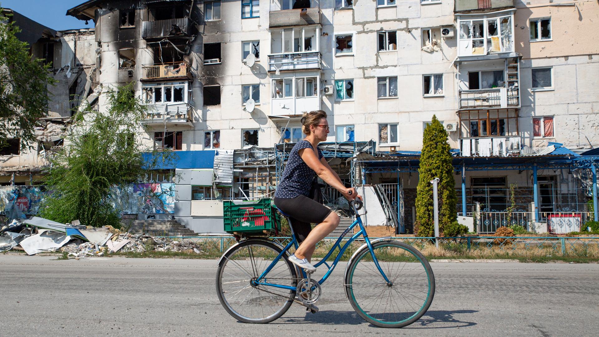 Eine Ukrainerin fährt mit dem Fahrrad an einem kriegszerstörten Häuserblock vorbei. Eine Ukrainerin fährt mit dem Fahrrad an einem kriegszerstörten Häuserblock vorbei.