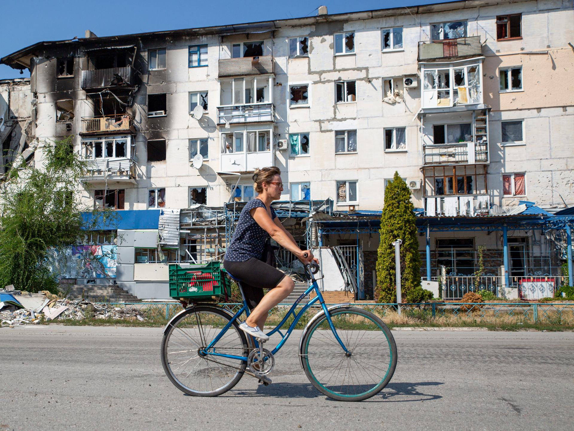 Eine Ukrainerin fährt mit dem Fahrrad an einem kriegszerstörten Häuserblock vorbei. 