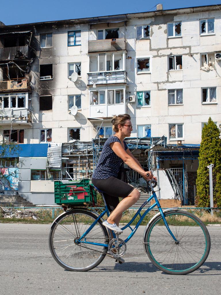 Eine Ukrainerin fährt mit dem Fahrrad an einem kriegszerstörten Häuserblock vorbei. 