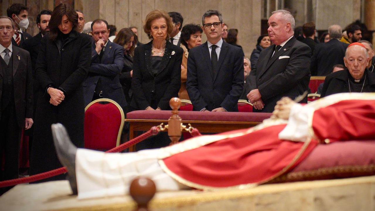 Sieben Menschen, darunter Sophia, die ehemalige Königin von Spanien, stehen hinter dem aufgebahrten Papst Benedikt.