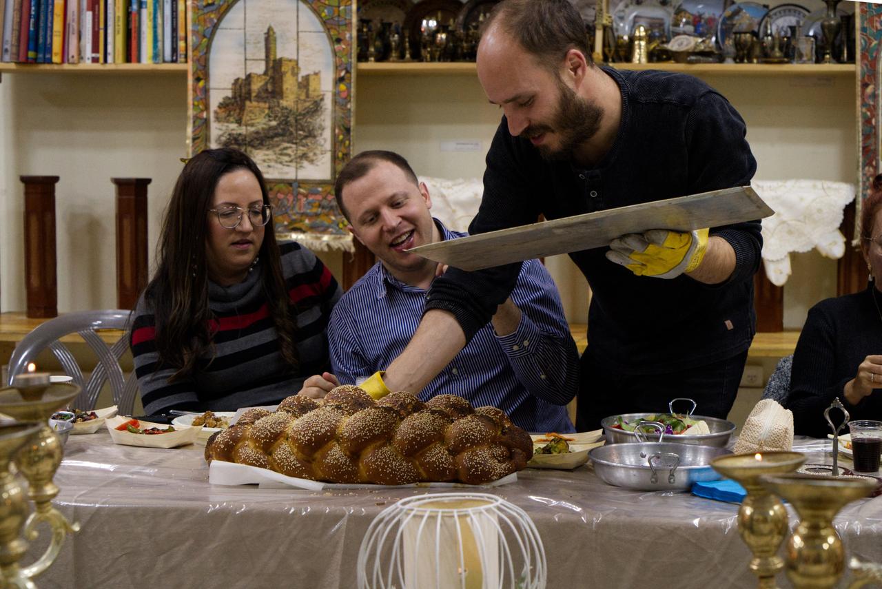 Zwei Männer und eine Frau freuen sich über ein mit Sesam bestreutes Brot, das frisch vom Backblech auf den Tisch kommt.