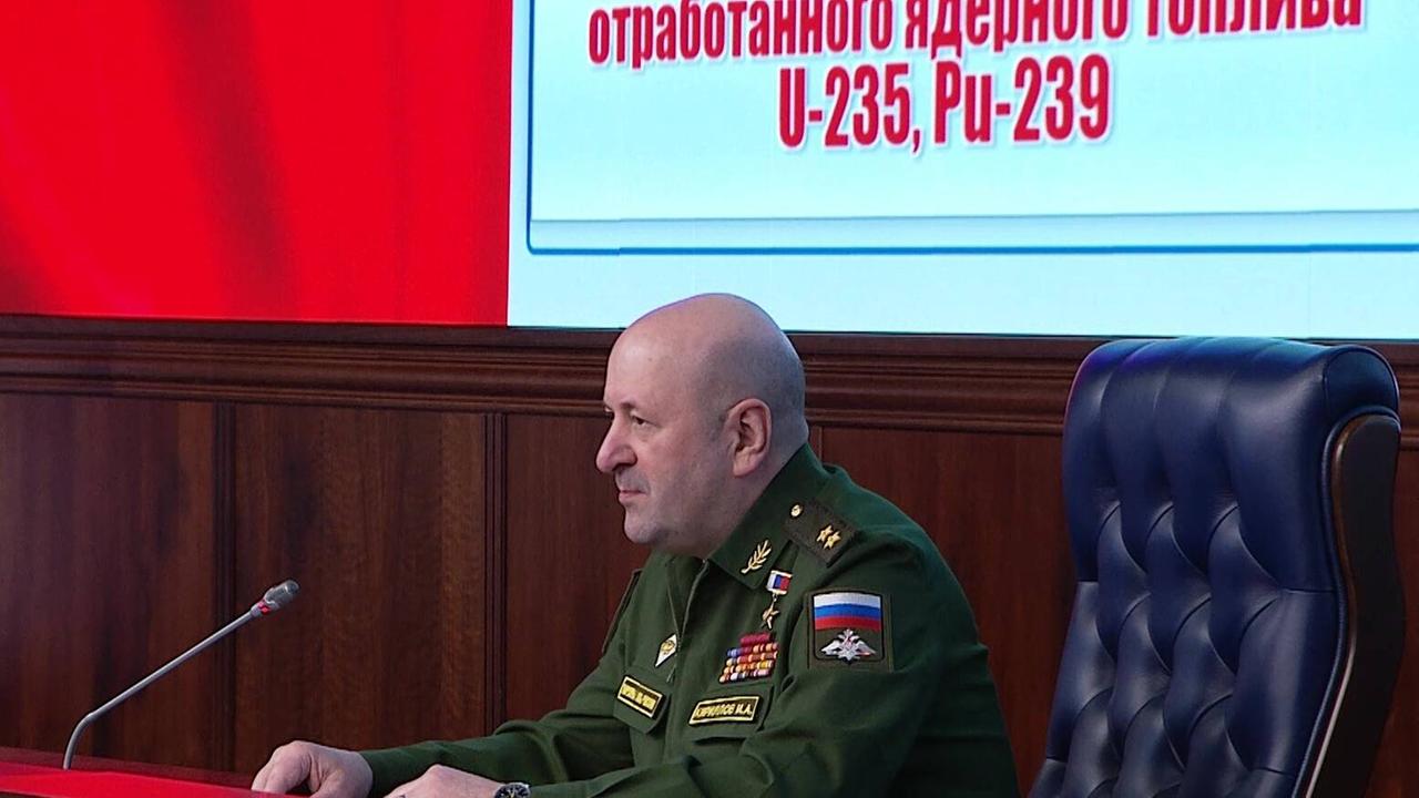Kirillov ist in Uniform schräg von der Seite fotogtrafiert. Er sitzt vor einer getäfelten Holzwand in einem Ledersessel. Über ihm eine hellblaue Projektionswand mit roter Schrift.