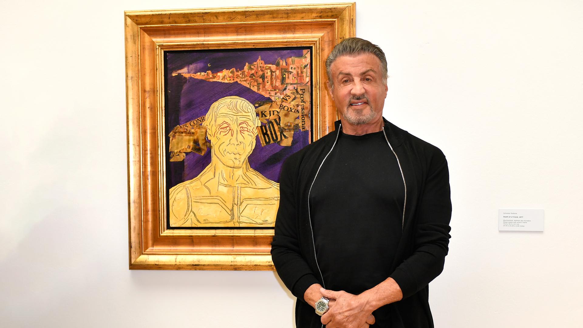 Der Schauspieler Sylvester Stallone steht vor seinem Bild "Finding Rocky". Er lächelt in die Kamera. Der Schauspieler Sylvester Stallone steht vor seinem Bild "Finding Rocky". Er lächelt in die Kamera.
