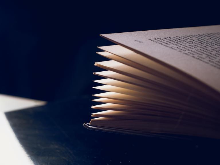 Geöffnetes und gefächertes Buch vor dunklem Hintergrund mit Textfreiraum