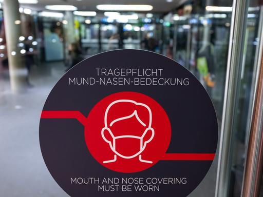 Ein Schild mit der Aufschrift "Tragepflicht Mund-Nasen-Bedeckung" ist an einer Tür eines Busbahnhofs zu sehen.