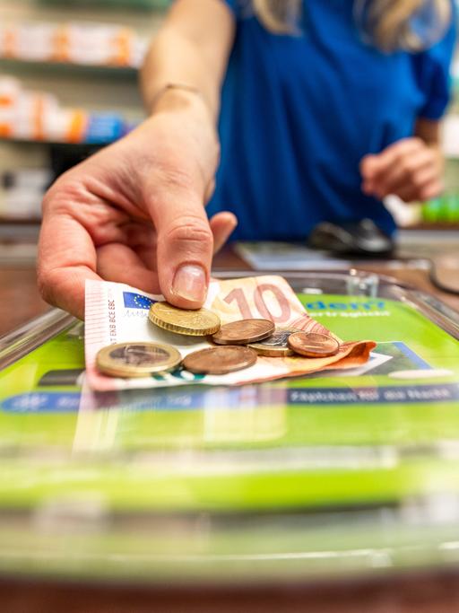Eine Mitarbeiterin nimmt 12,71 Euro von einem Tresen in der Markt-Apotheke.