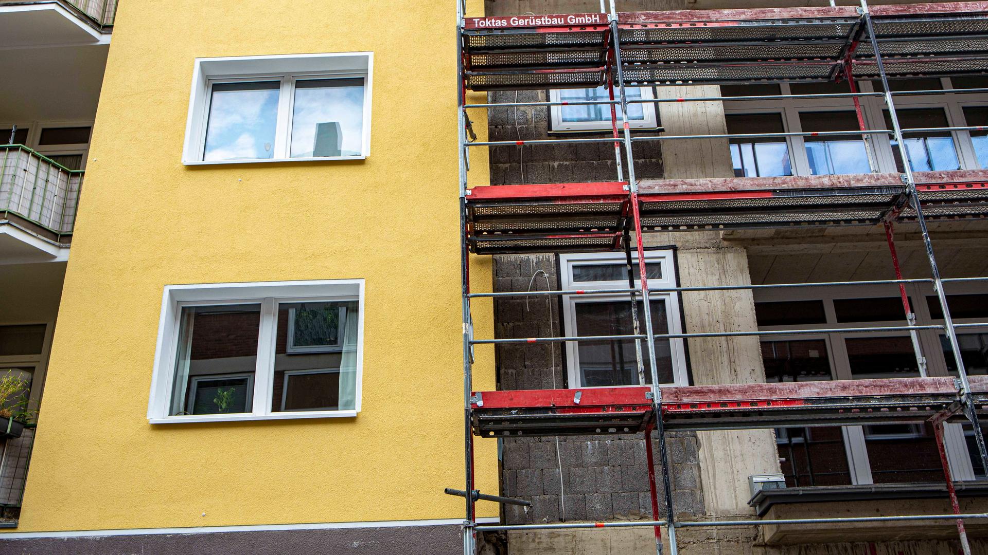 Eine Gerüst steht an einem Gebäude, das saniert wird, neben einem bereits renovierten Gebäude.