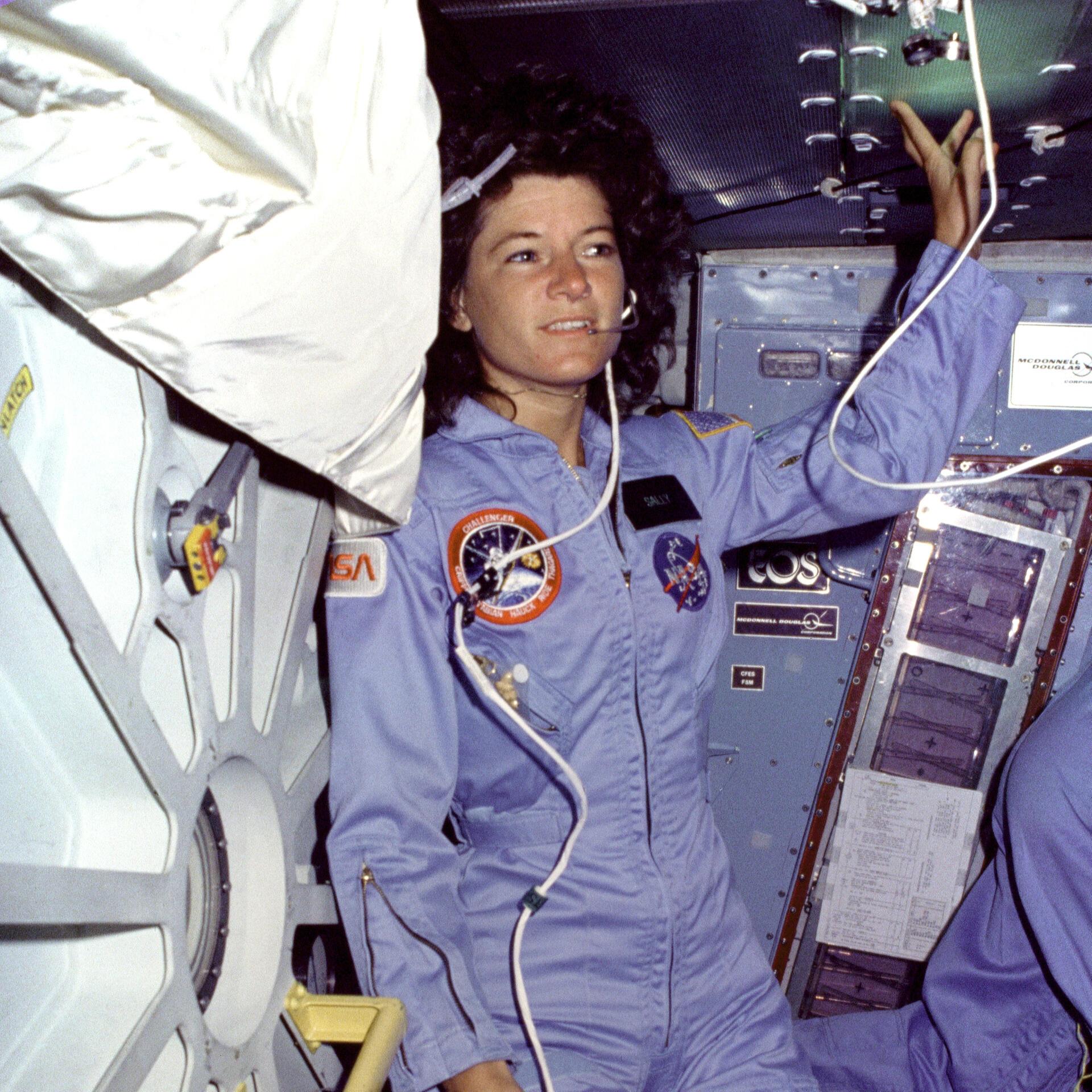 Sally Ride trägt auf einer Raumstation einen blauen Overall und ein Headset.