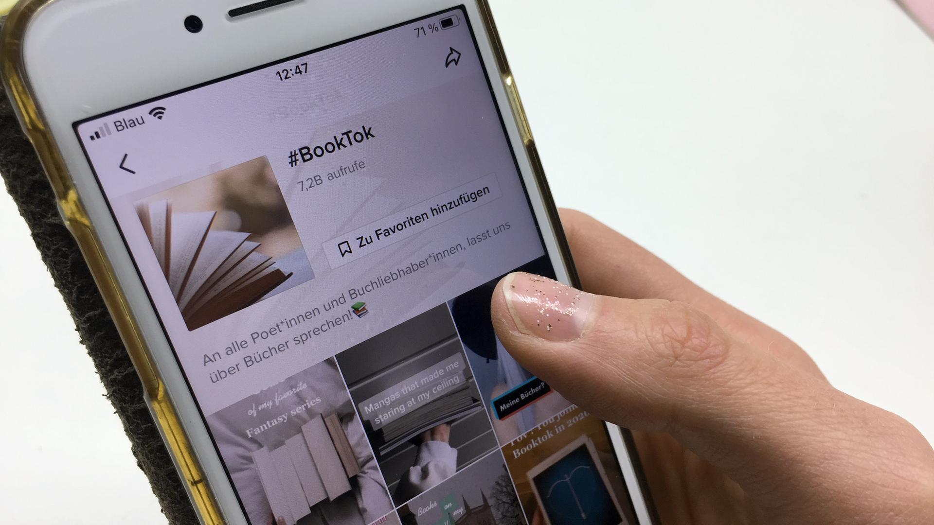 Eine Hand hält ein Smartphone, auf dem die Plattform #BookTook mit Buchempfehlungen bei TikTok geöffnet ist. Eine Hand hält ein Smartphone, auf dem die Plattform #BookTook mit Buchempfehlungen bei TikTok geöffnet ist.