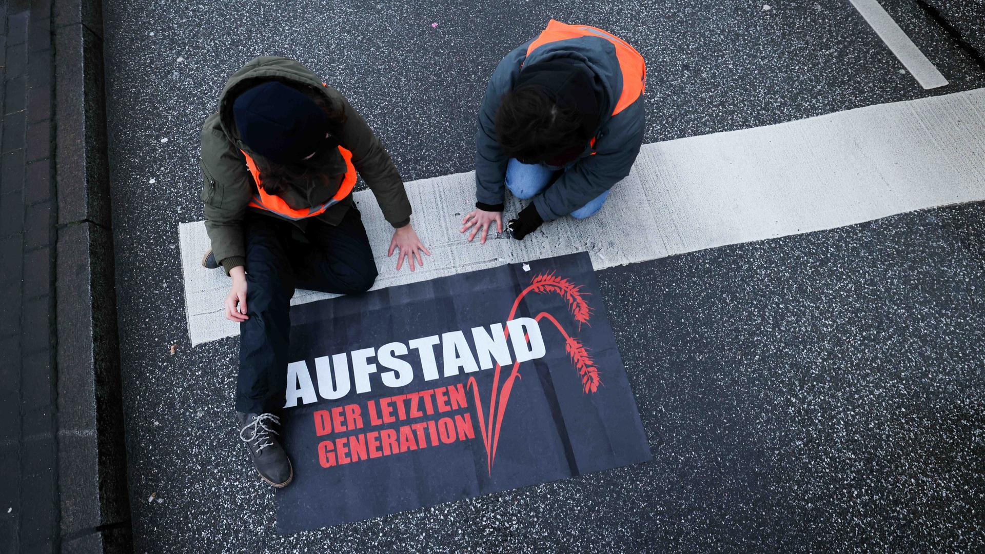 Klimaaktivisten der Gruppe "Aufstand der letzten Generation" haben ihre Hände in Hamburg auf die Straße geklebt. Neben ihnen liegt ein Transparent mit der Aufschrift: "Aufstand der letzten Generation". Klimaaktivisten der Gruppe "Aufstand der letzten Generation" haben ihre Hände in Hamburg auf die Straße geklebt. Neben ihnen liegt ein Transparent mit der Aufschrift: "Aufstand der letzten Generation".