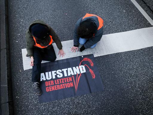 Klimaaktivisten der Gruppe "Aufstand der letzten Generation" haben ihre Hände in Hamburg auf die Straße geklebt. Neben ihnen liegt ein Transparent mit der Aufschrift: "Aufstand der letzten Generation".
