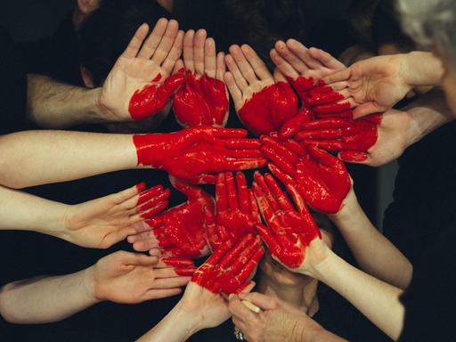 Auf mehrere Hände gemalte rote Farbe stellt ein Herz dar. (Symbolfoto)