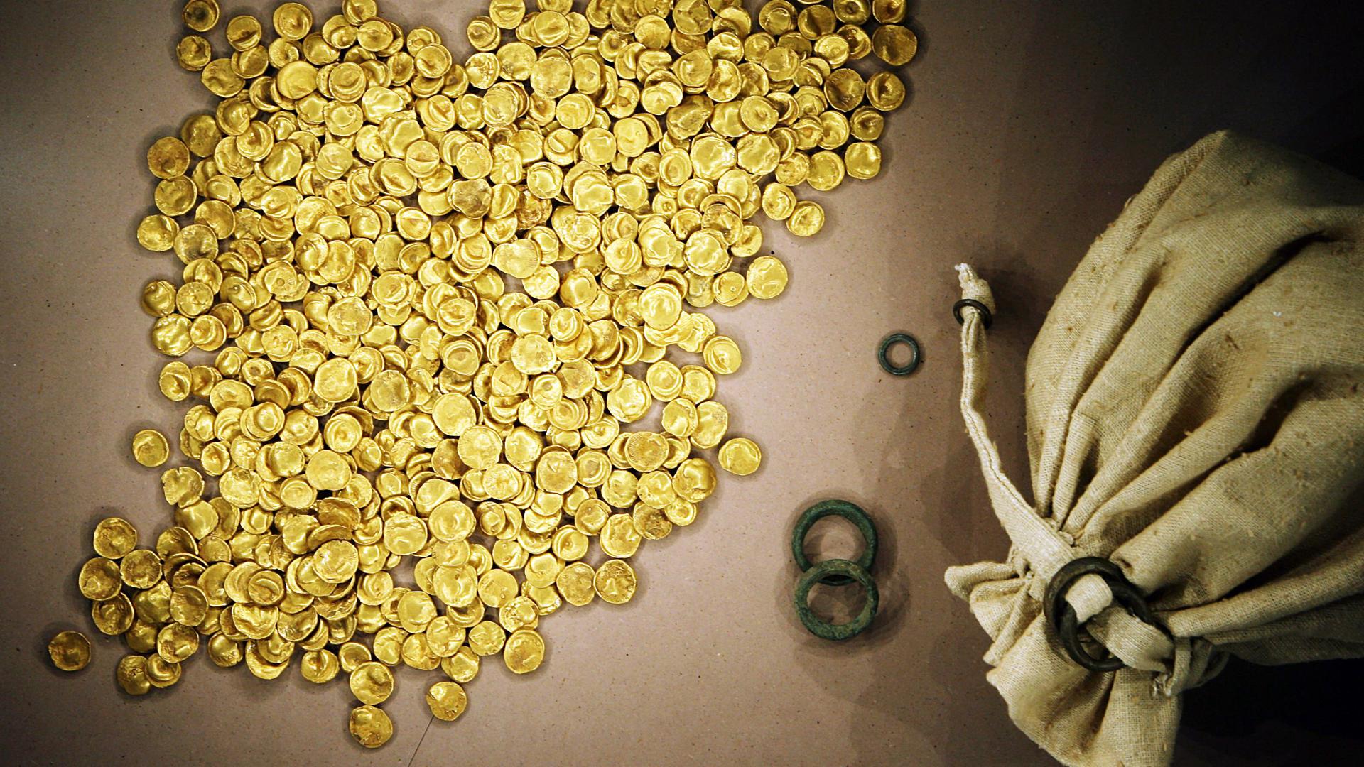Viele Gold-Münzen liegen neben einem offenen Stoff-Beutel. Viele Gold-Münzen liegen neben einem offenen Stoff-Beutel.