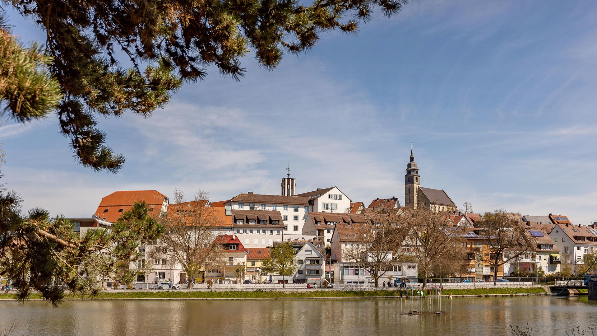 Stadtansicht von Böblingen mit blauem Himmel. Im Bildvordergrund ist der Untere See zu sehen, vom linken Bildrand ragt ein großer Ast eines Nadelbaums ins Bild. Stadtansicht von Böblingen mit blauem Himmel. Im Bildvordergrund ist der Untere See zu sehen, vom linken Bildrand ragt ein großer Ast eines Nadelbaums ins Bild.