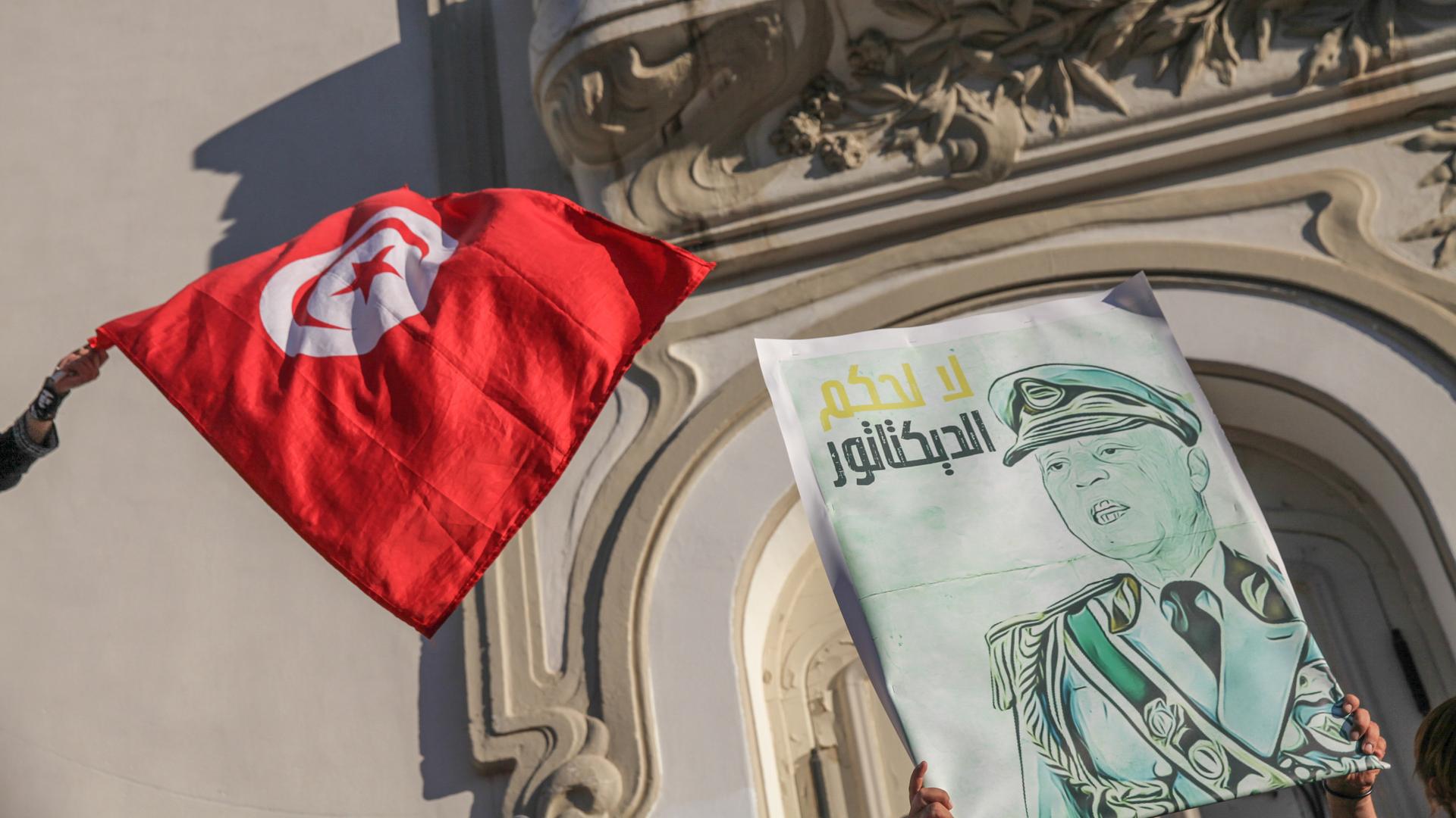 Eine Karikatur des tunesischen Präsidenten Kais Saied in Militäruniform mit der arabischen Aufschrift "Nein zur Herrschaft eines Diktators" neben der tunesischen Flagge. Während einer Demonstration von Anhängern tunesischer Oppositionsparteien und tunesischer zivilgesellschaftlicher Gruppen in Tunis am 22. Juli 2022, um gegen den tunesischen Präsidenten Kais Saied zu protestieren und zum Boykott des bevorstehenden Verfassungsreferendums am 25. Juli aufzurufen. Eine Karikatur des tunesischen Präsidenten Kais Saied in Militäruniform mit der arabischen Aufschrift "Nein zur Herrschaft eines Diktators" neben der tunesischen Flagge. Während einer Demonstration von Anhängern tunesischer Oppositionsparteien und tunesischer zivilgesellschaftlicher Gruppen in Tunis am 22. Juli 2022, um gegen den tunesischen Präsidenten Kais Saied zu protestieren und zum Boykott des bevorstehenden Verfassungsreferendums am 25. Juli aufzurufen.