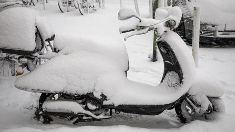 Ein verschneiter Motorroller steht am Straßenrand.