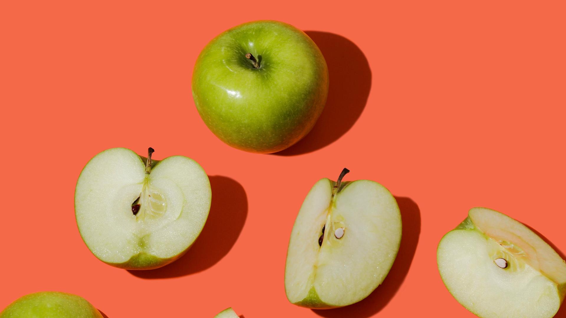 Verschiedene grüne Äpfel, einige aufgeschnitten, andere ganz, auf rot-orangefarbenem Hintergrund. Verschiedene grüne Äpfel, einige aufgeschnitten, andere ganz, auf rot-orangefarbenem Hintergrund.
