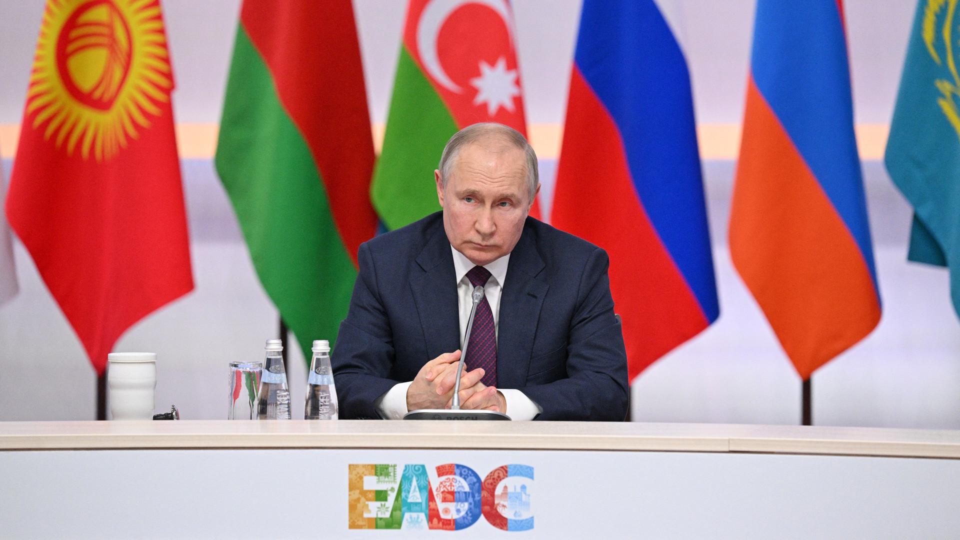 Russlands Präsident Putin sitzt an einem Tisch, im Hintergrund mehrere Flaggen, darunter die russische. Russlands Präsident Putin sitzt an einem Tisch, im Hintergrund mehrere Flaggen, darunter die russische.