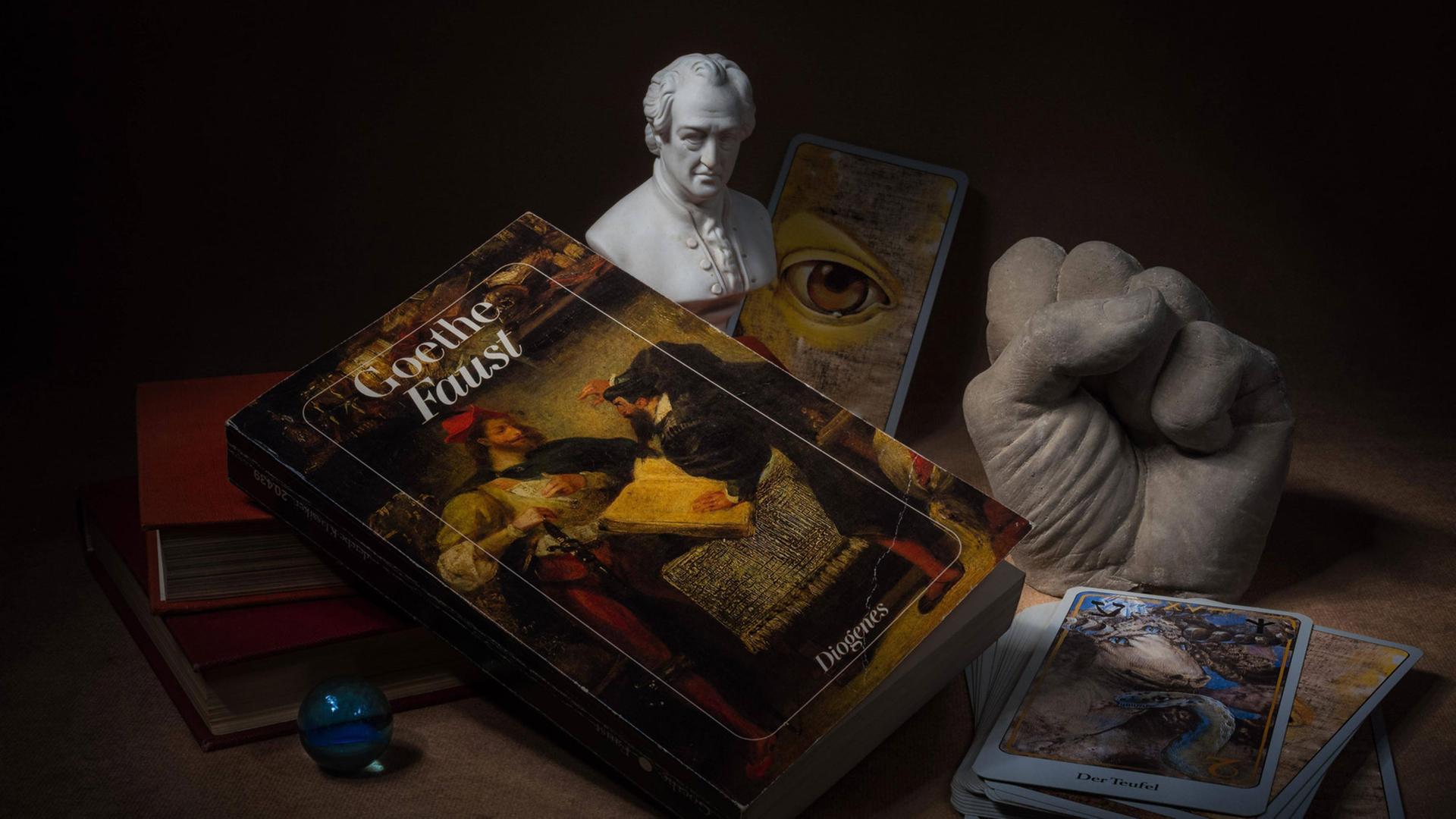 Hörspielkomödie über Goethes "Faust" und die Mühen des Deutschwerdens. Zu sehen: Stilleben mit Büchern, Glaskugel, Tarotkarten, Goethe-Büste, das Buch "Faust" und einer Plastikhand zu einer Faust geballt. Hörspielkomödie über Goethes "Faust" und die Mühen des Deutschwerdens. Zu sehen: Stilleben mit Büchern, Glaskugel, Tarotkarten, Goethe-Büste, das Buch "Faust" und einer Plastikhand zu einer Faust geballt.