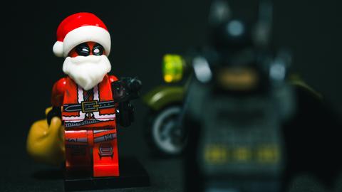 Ein böse blickender Lego-Weihnachtsmann richtet eine Pistole auf eine andere Lego-Figur, die verschwommen im Vordergrund steht.