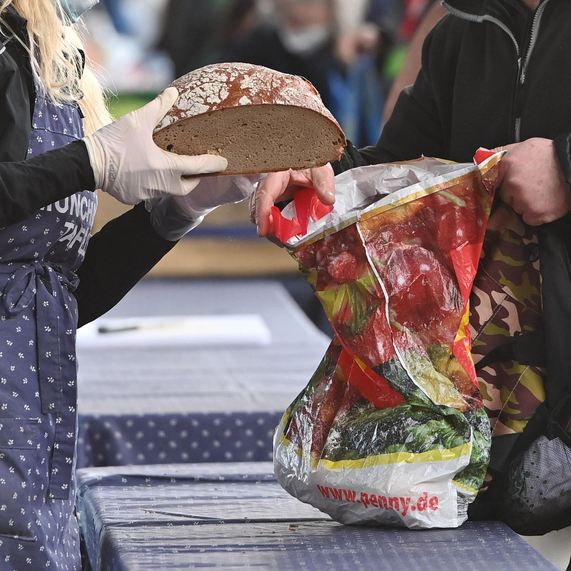 Bedürftige Menschen bei einer Tafel bei der Ausgabe von Lebensmitteln, ein Brot wird in eine Plastiktüte gesteckt.