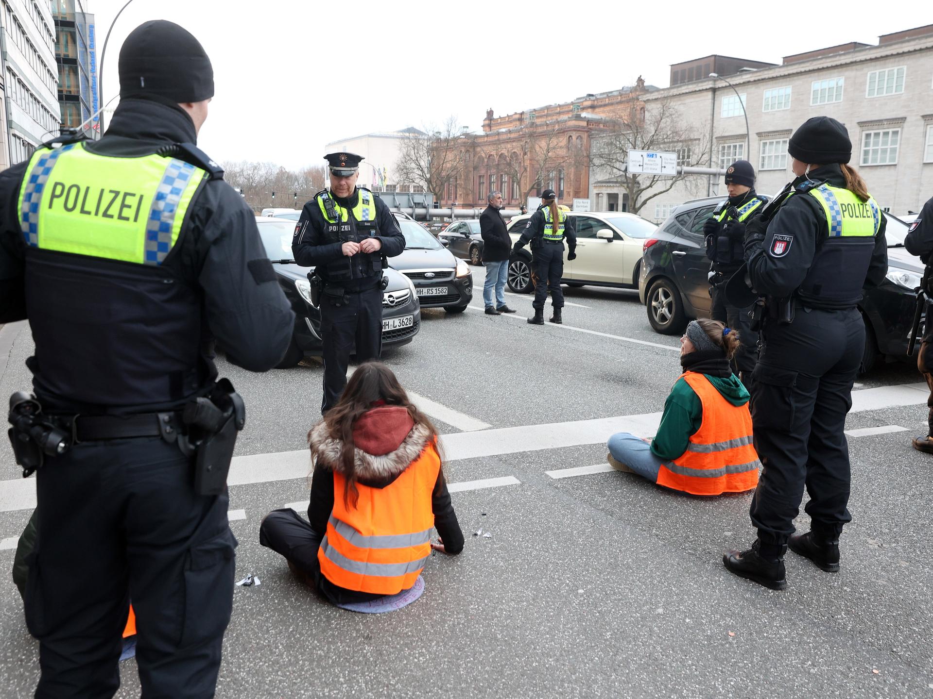 Klimaaktivisten blockieren eine Straße in Hamburg. Sie sind umringt von Polizisten, vor ihnen stauen sich Autos. (Symbolbild)