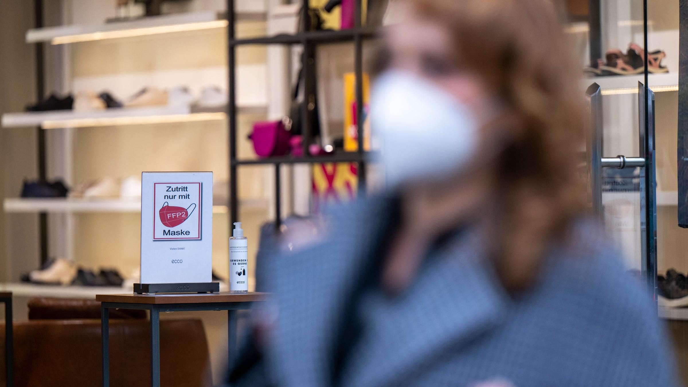 Ein Schild am Eingang eines Schuh-Geschäfts in der City-West weist auf die Pflicht zum Tragen einer FFP2-Maske hin, während im Vordergrund eine Frau mit FFP2-Maske vorbeigeht. Seit 18. Februar entfällt in Berlin die 2G-Regel für den gesamten Einzelhandel.