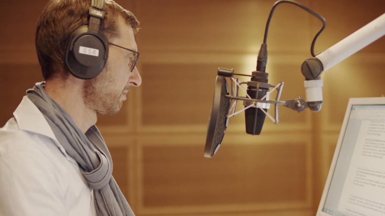 Ein Mann sitzt in einem Aufnahmestudio vor einem Mikrofon und trägt Kopfhörer