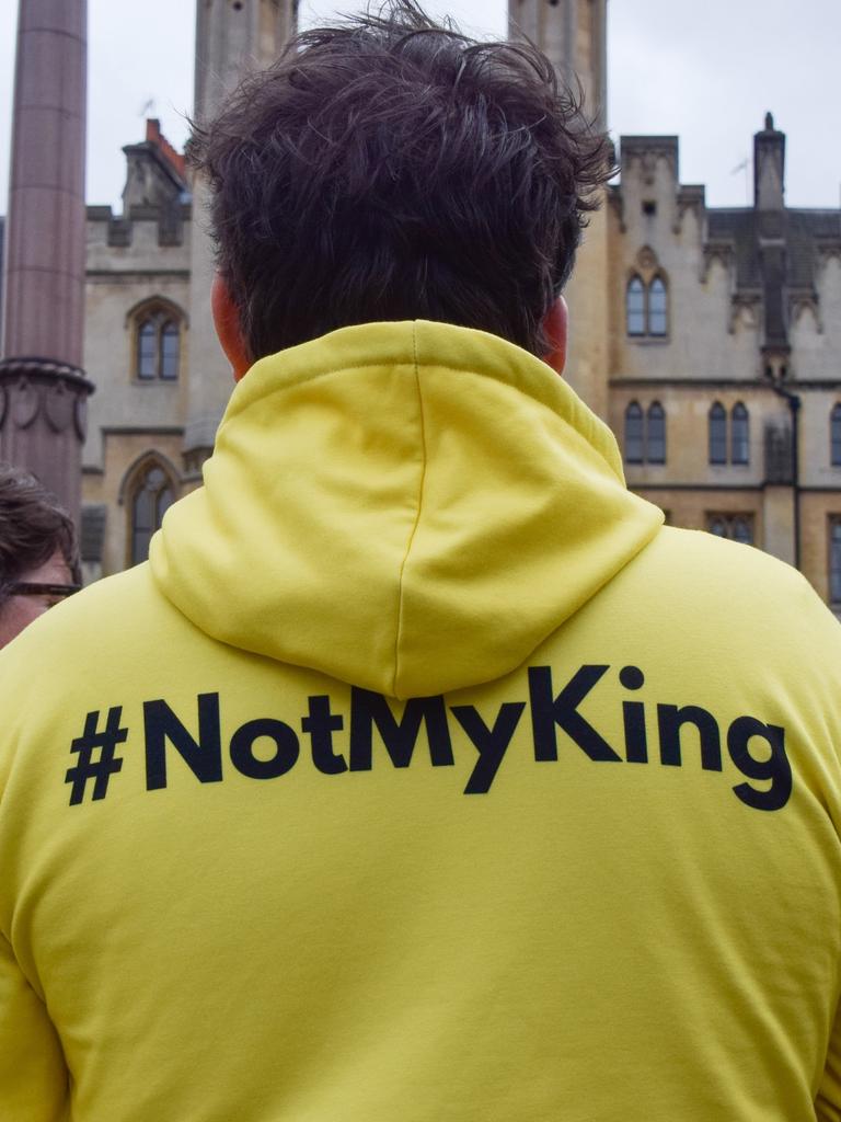 Eine Person, die einen neongelben Pullover mit der Aufschrift "#notmyking" trägt steht zusammen mit anderen Personenn vor einem Gebäude in London